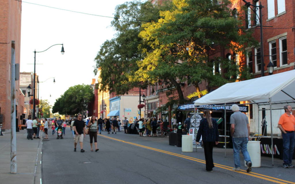 A city street during a festival with tents and many people walking around